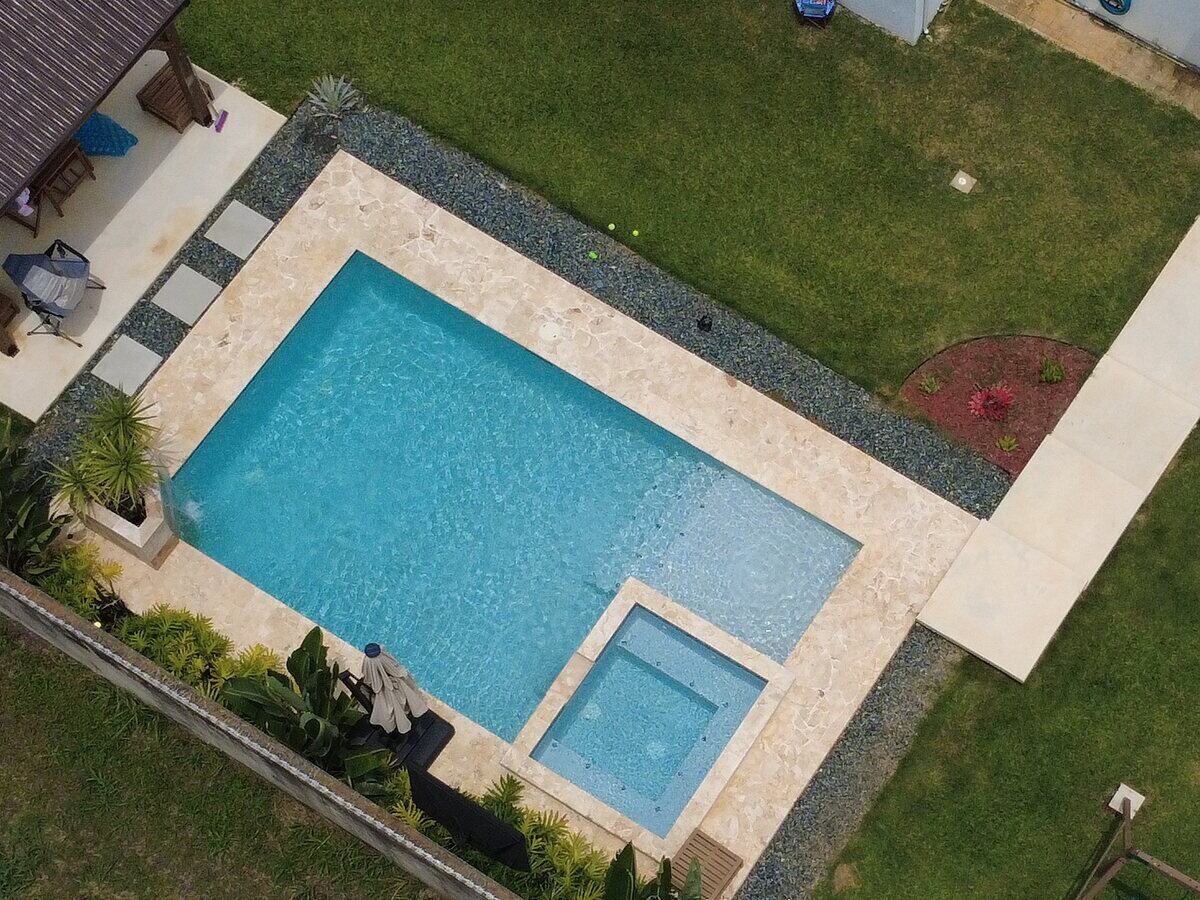 Vista aérea de una piscina construida por Forze Corp. con jacuzzi integrado y deck de travertino