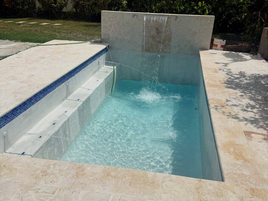 Piscina terminada con cascada sobre muro y aceras de travertino